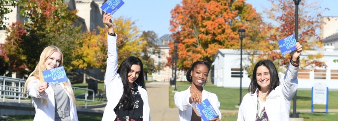 Pharmacy students outside Pharmacy Building holding "Here is Where Great Health Care Leaders are Created" post cards. 