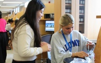 Zoom image: Student leader guiding a PSI student administering a mock vaccination. 