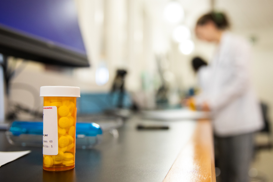 Prescription medication bottle on a pharmacy counter with a student pharmacist working in the background. 